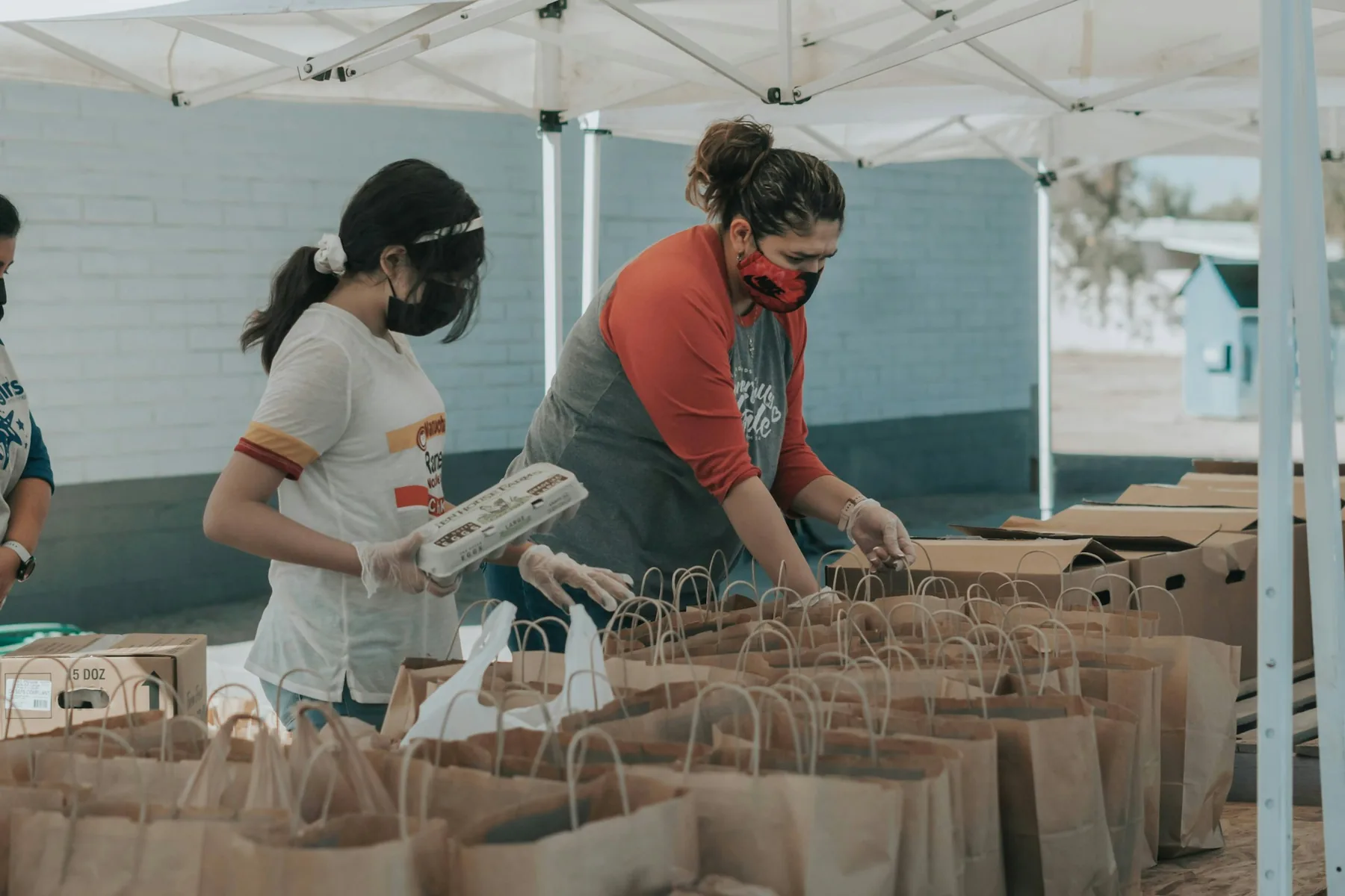 Volunteers prepare food bags together at an outdoor distribution table.